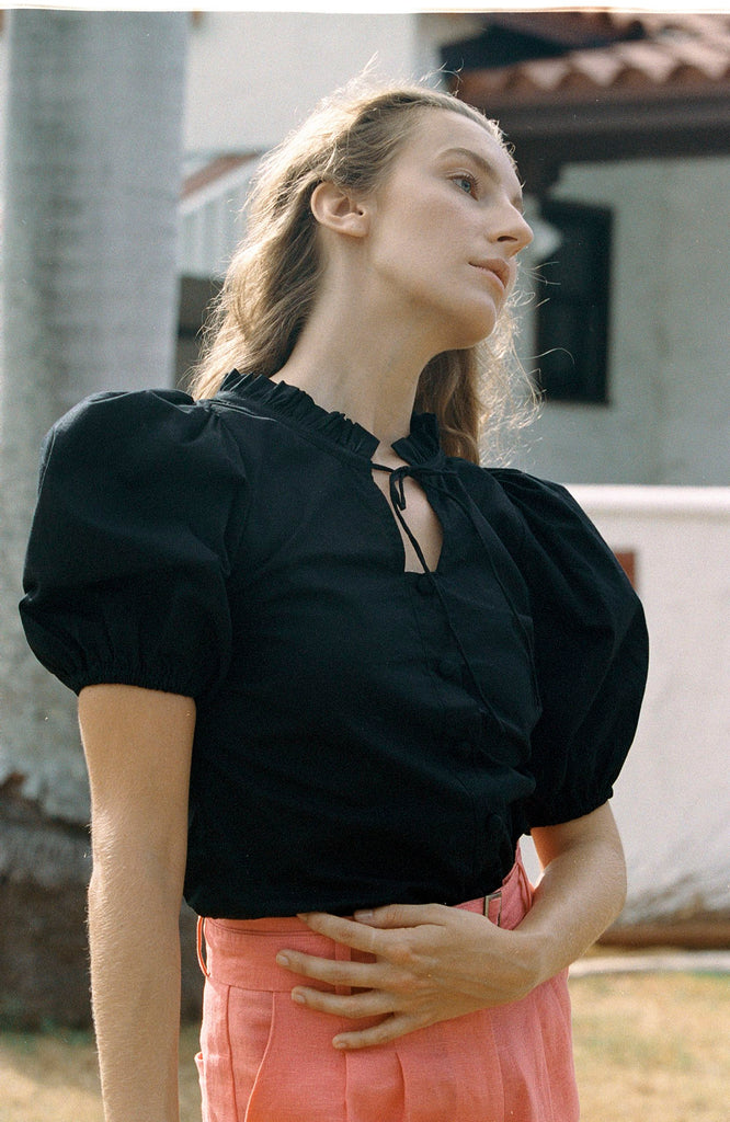 Black cotton puff-sleeve blouse with buttons paired with salmon colored pants